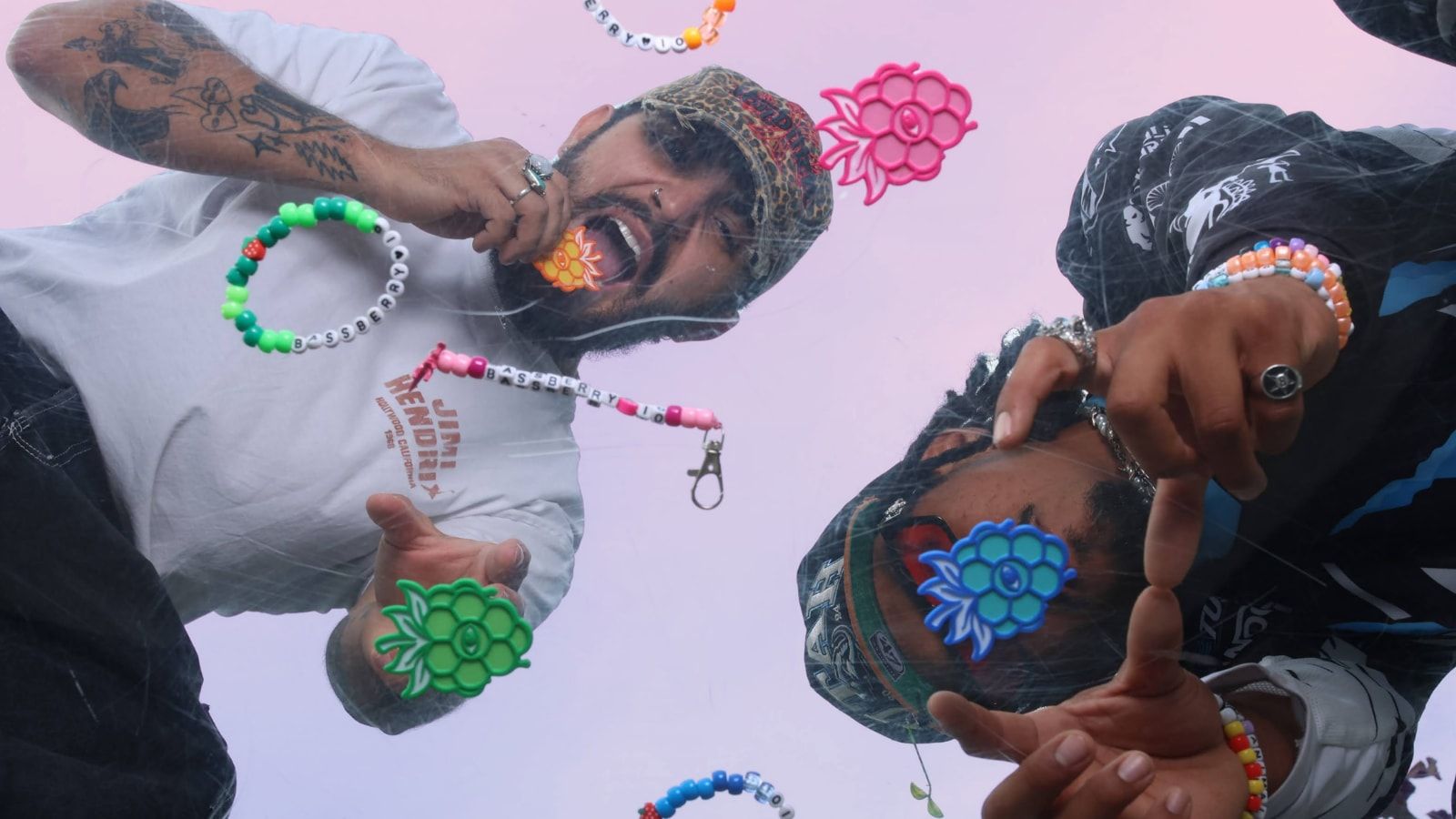 Two people at a festival, framed upside down, each with a berry — one held to their mouth, one resting over their eye.